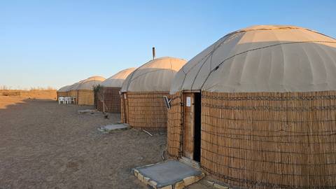       Row of traditional yurts in a desert landscape during sunset.
  