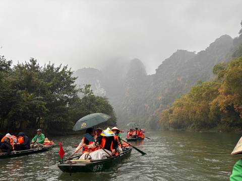       Tourists in boats along a river surrounded by misty mountains.
  