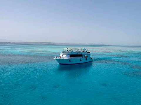 Boat cruising on pristine blue water with sandy landscape.