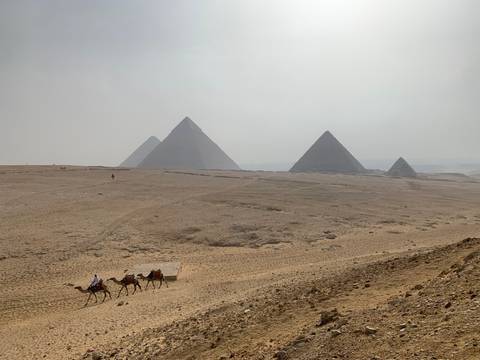 Pyramids in the desert landscape with distant camels.