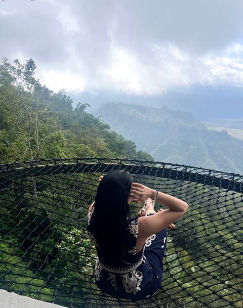 Person enjoying a view from a netted lookout with lush forests and mountains.
