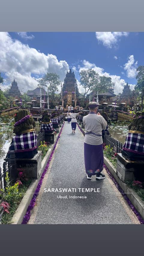 People in traditional attire walking on a path flanked by statues in a temple.