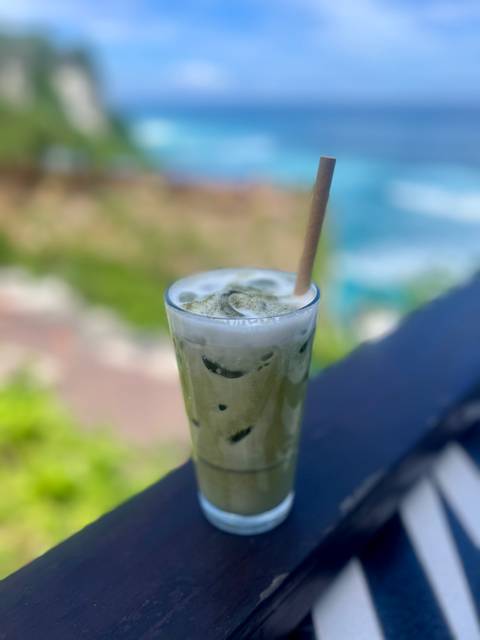      Close-up of an iced matcha drink on a table with ocean view.
  