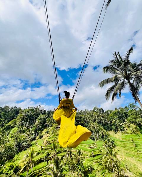 Woman in a yellow dress on a swing over lush greenery.