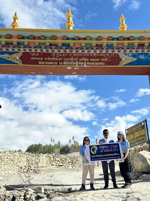       Three people standing under a decorated archway with a sign for Lo-Manthang.
  