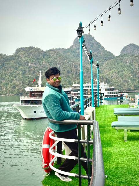 Man in a teal jacket enjoying a cruise with boats in the background.