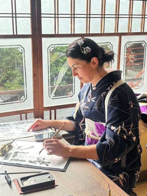       A woman engaged in traditional calligraphy in a serene setting.
  