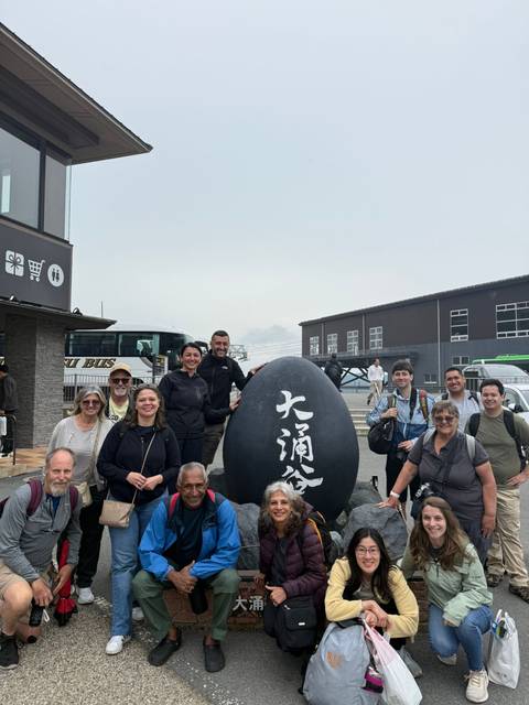       Group of tourists posing with a large black stone egg at a tourist site.
  