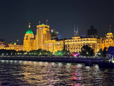       Night view of the Bund in Shanghai with illuminated buildings and reflections on the river.
  