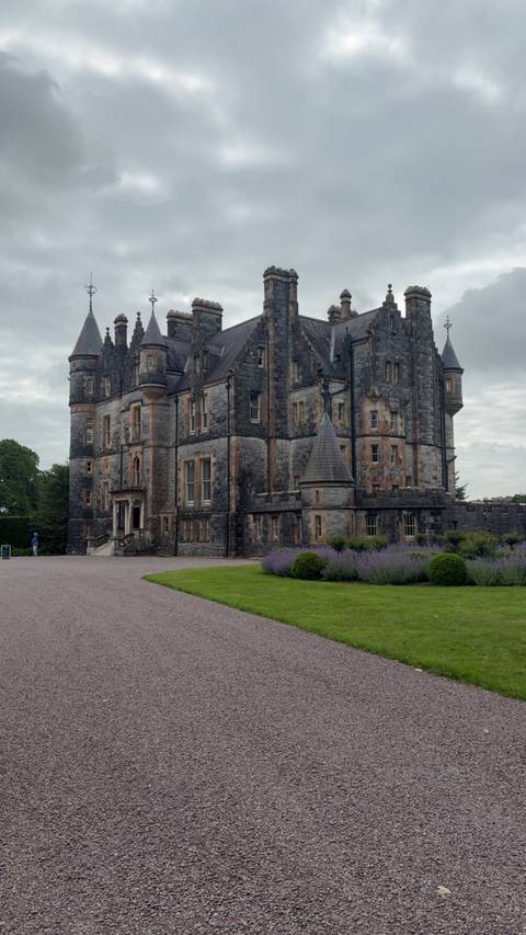 Large historic stone castle with gardens and a cloudy sky.