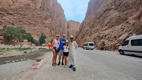       Family posing in a desert canyon with a road and parked vehicles, possibly in Boumalne Dades, Morocco.
  