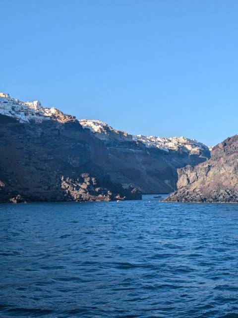       Coastal village with white buildings on a rocky cliff by the sea, likely Santorini, Greece.
  