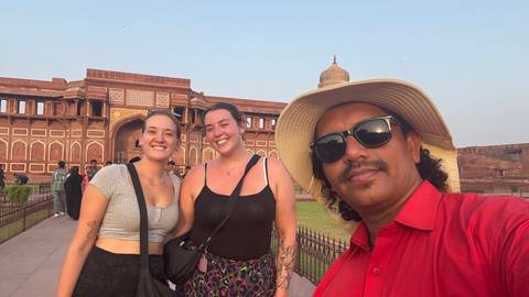 Three people standing in front of an ancient fort during sunset.