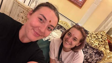       Two women with traditional forehead marks sitting indoors.
  