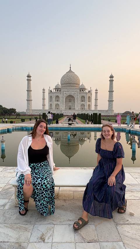       Two women visiting Taj Mahal with reflection in the background.
  
