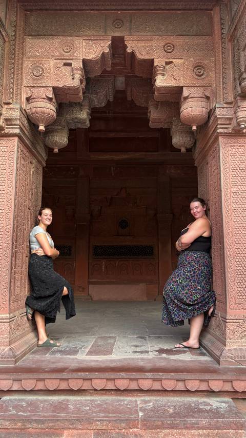 Two women standing in front of intricately carved stone walls.