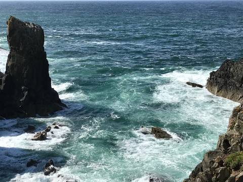 Rocky coastline with waves crashing against the rocks and clear blue water.