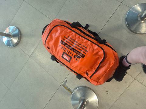       Close-up of an orange duffel bag on airport floor.
  
