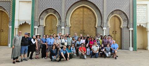       Group posing in front of an ornate entrance with golden doors.
  