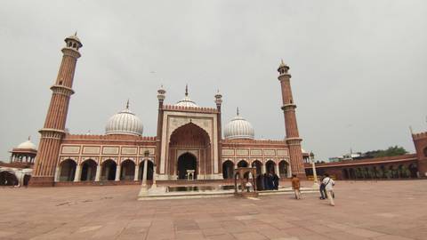       A large mosque with domes and people walking in the courtyard.
  