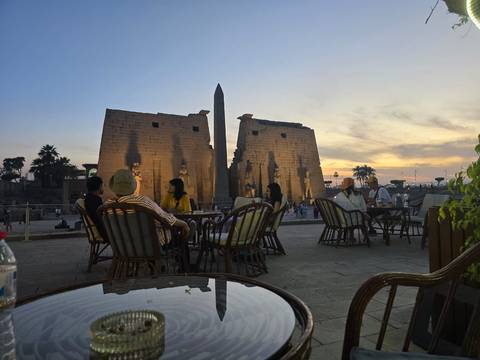 Outdoor café with people in front of historical ruins at sunset.