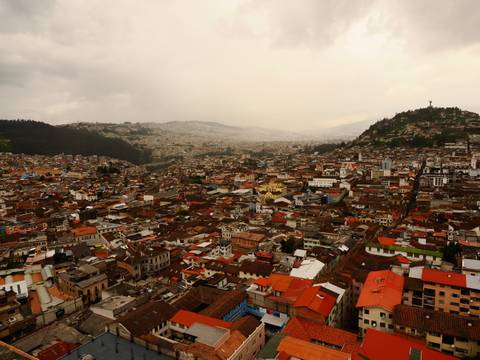       Panoramic view of a city with hills and a cloudy sky.
  