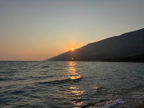 A scenic sunset over the sea with dark hills in the background.