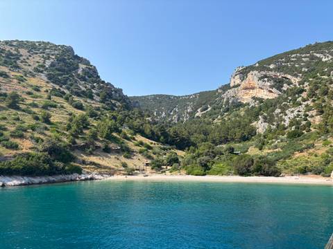 A secluded beach surrounded by green hills and clear blue water.