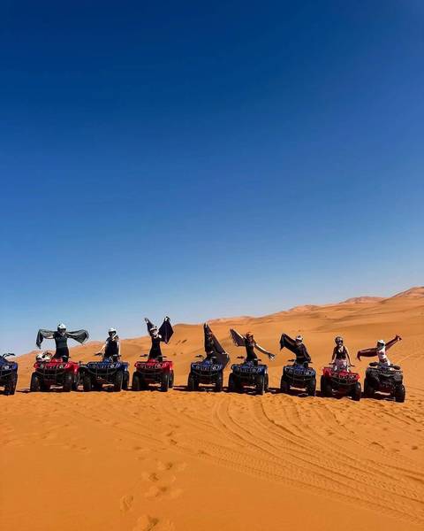 Group riding quad bikes in the desert, posing with arms raised.