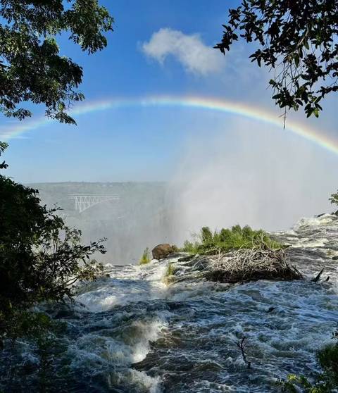 A rainbow over Victoria Falls with a view of a bridge.