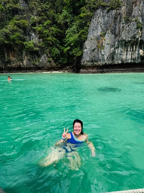       A woman smiling in green water with cliffs in the background.
  