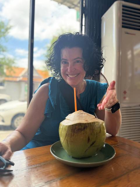 A woman sitting with a coconut drink, pointing at it.