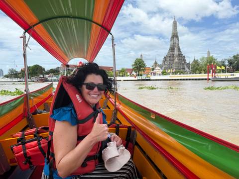       A woman giving a thumbs up while on a boat with a temple in the background.
  