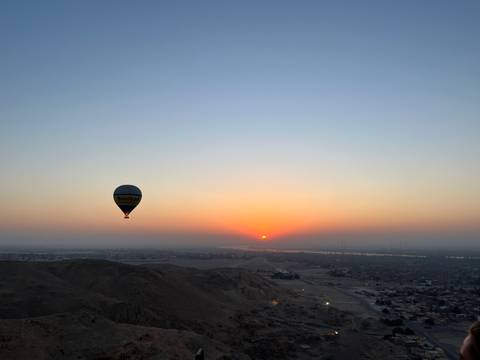 Balloon floating over a desert landscape during sunrise.