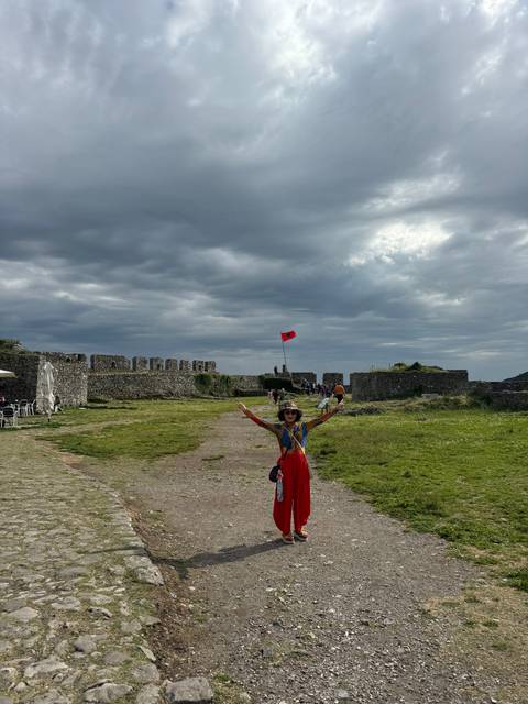 Tourist raising arms in front of an old fortress with a flag.