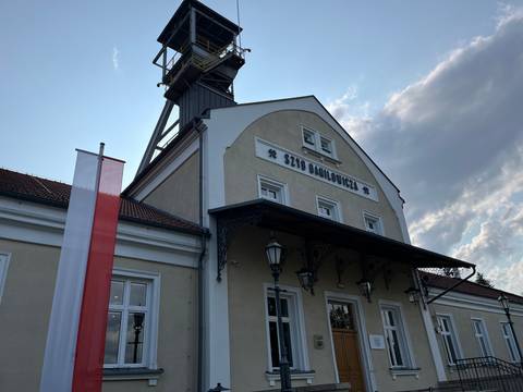       Entry to a building with a tall structure and Polish flags.
  