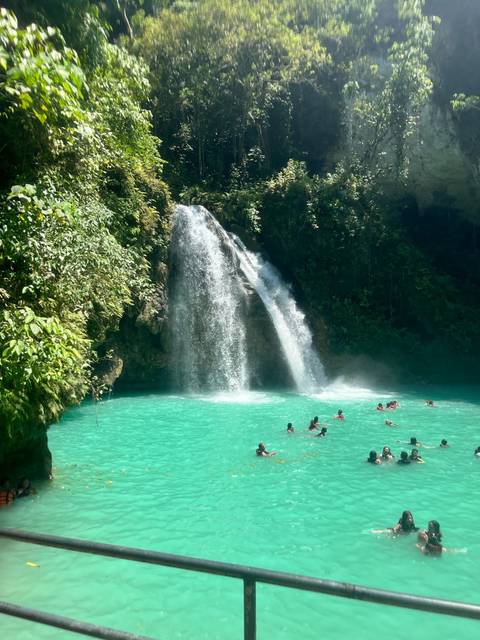 A waterfall cascading into a turquoise pool with people swimming.