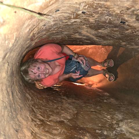 A person crouching in a narrow, historical underground tunnel smiling at the camera.
