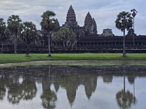       A view of Angkor Wat reflecting on a calm lake under a cloudy sky.
  
