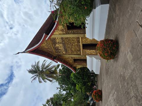       A traditional temple with intricate golden detailing surrounded by lush palm trees.
  