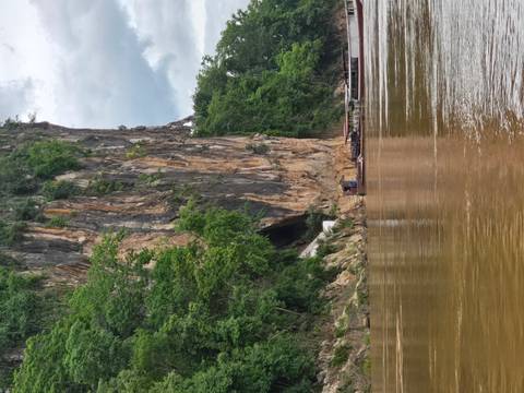 A rocky cliff face with a large cave opening, viewed from a river.