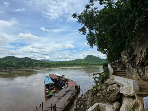       Two boats docked by a riverside with mountainous backdrop.
  