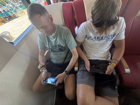      Two people sitting indoors and looking at their phones.
  