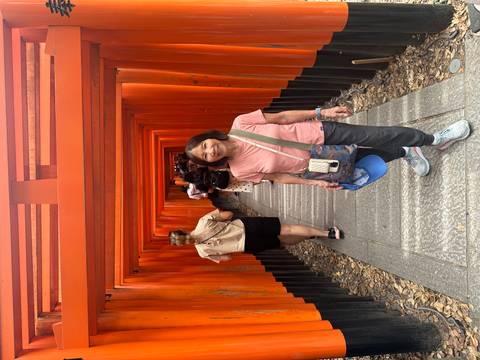       Tourist smiling in a corridor lined with red wooden torii gates.
  
