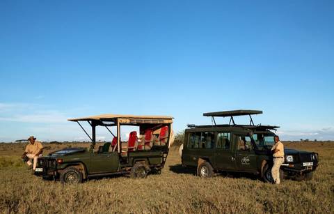 Two safari vehicles parked on a plain with people around