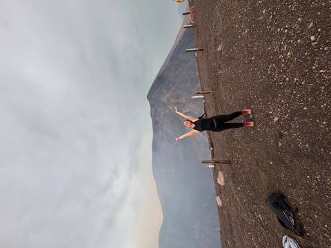 Person posing with arms raised in front of a volcanic landscape.