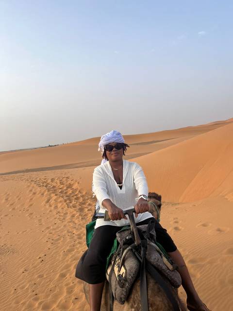 Person riding a camel with desert dunes in the background.