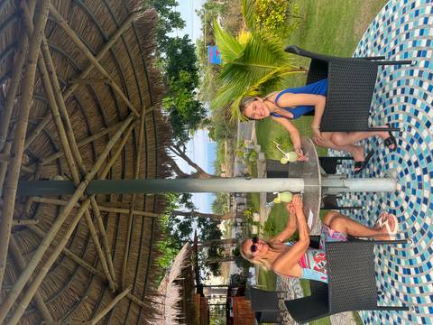       Two people enjoying drinks under a thatched shelter.
  