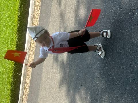       Child in uniform holding flags, posing playfully.
  