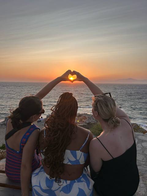 Silhouette of people forming a heart shape with hands at sunset by the sea.